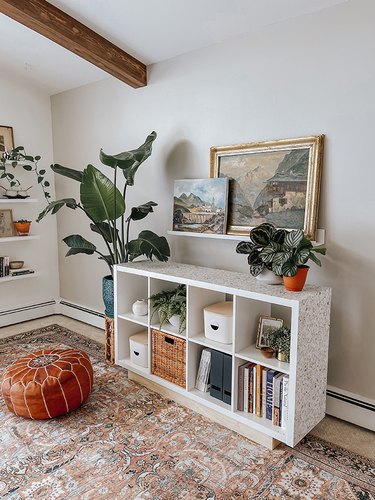 Ikea bookcase with terrazzo wallpaper, accented with plants, paintings, storage containers, and a leather floor cushion